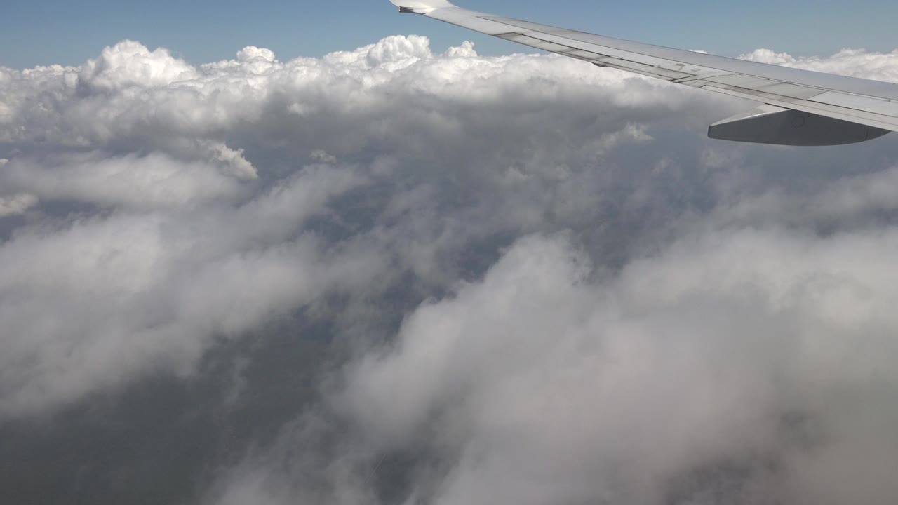 Airplane wing above thick clouds and blue sky.