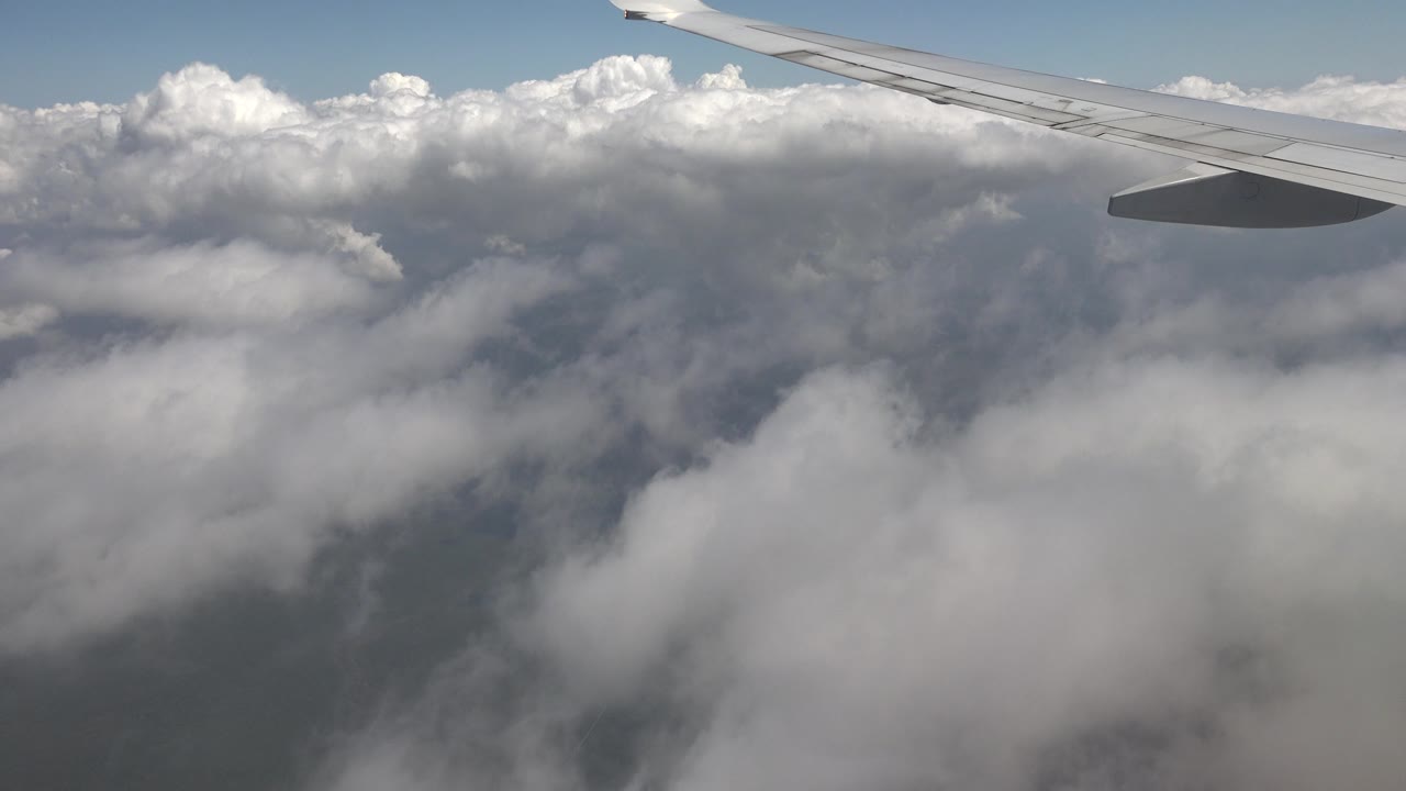 Airplane wing remains near the top edge while white and gray cloud banks fill the view over Playa del Carmen, Mexico, with no visible people.