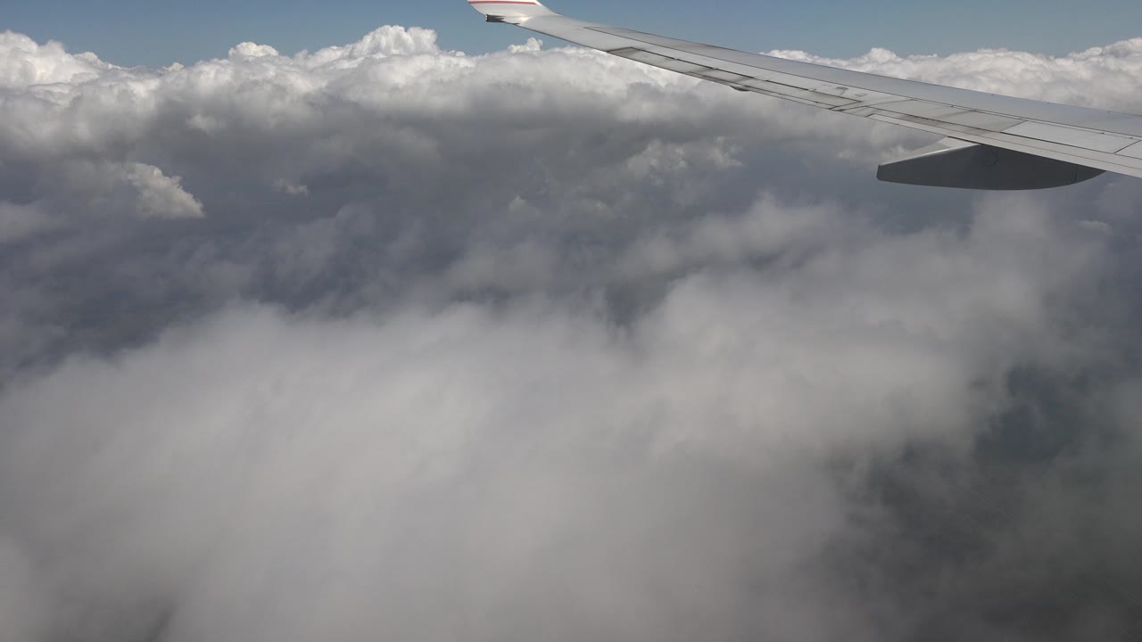 Airplane wing crossing bright cloud tops