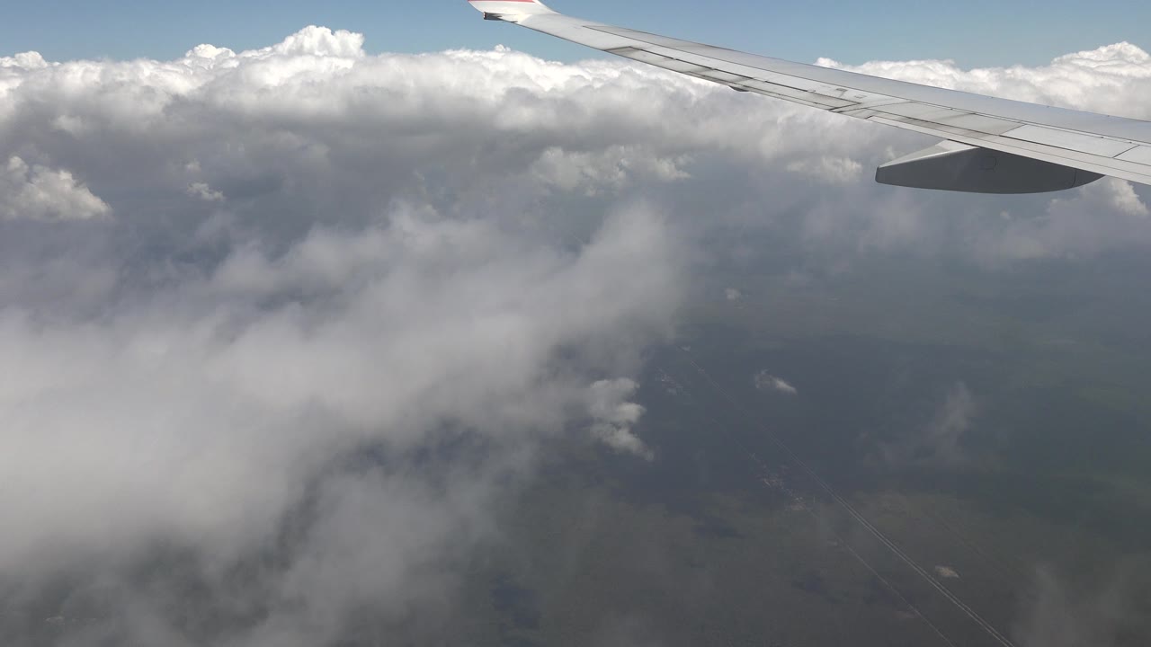 Airplane wing above clouds and distant land.