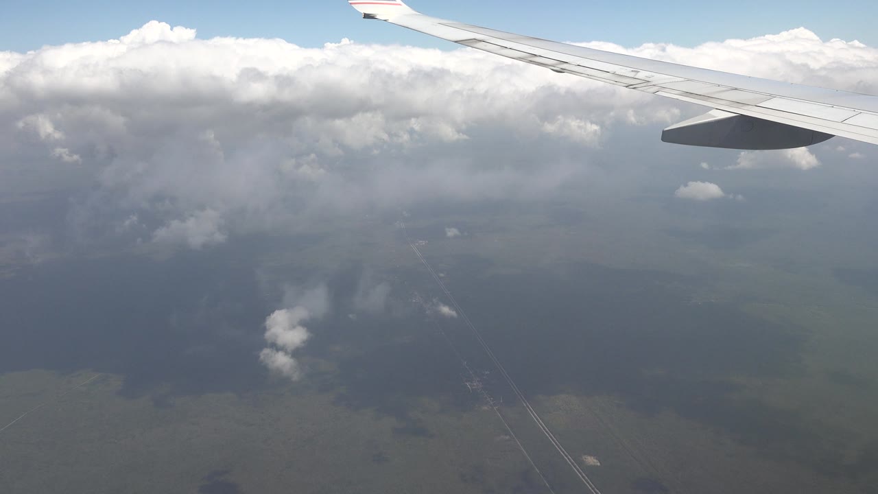 Airplane wing with clouds and faint ground below