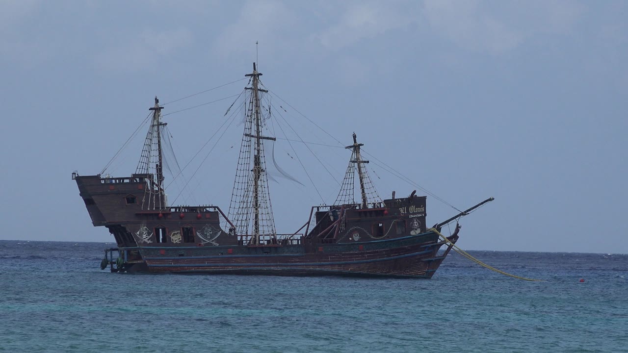 Pirate-style ship floating on blue ocean water under a pale sky.