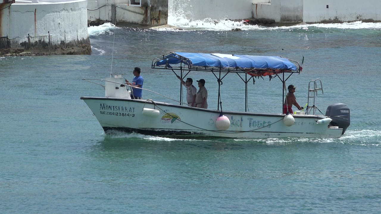 White canopy boat carrying four men on turquoise water near a white seawall.