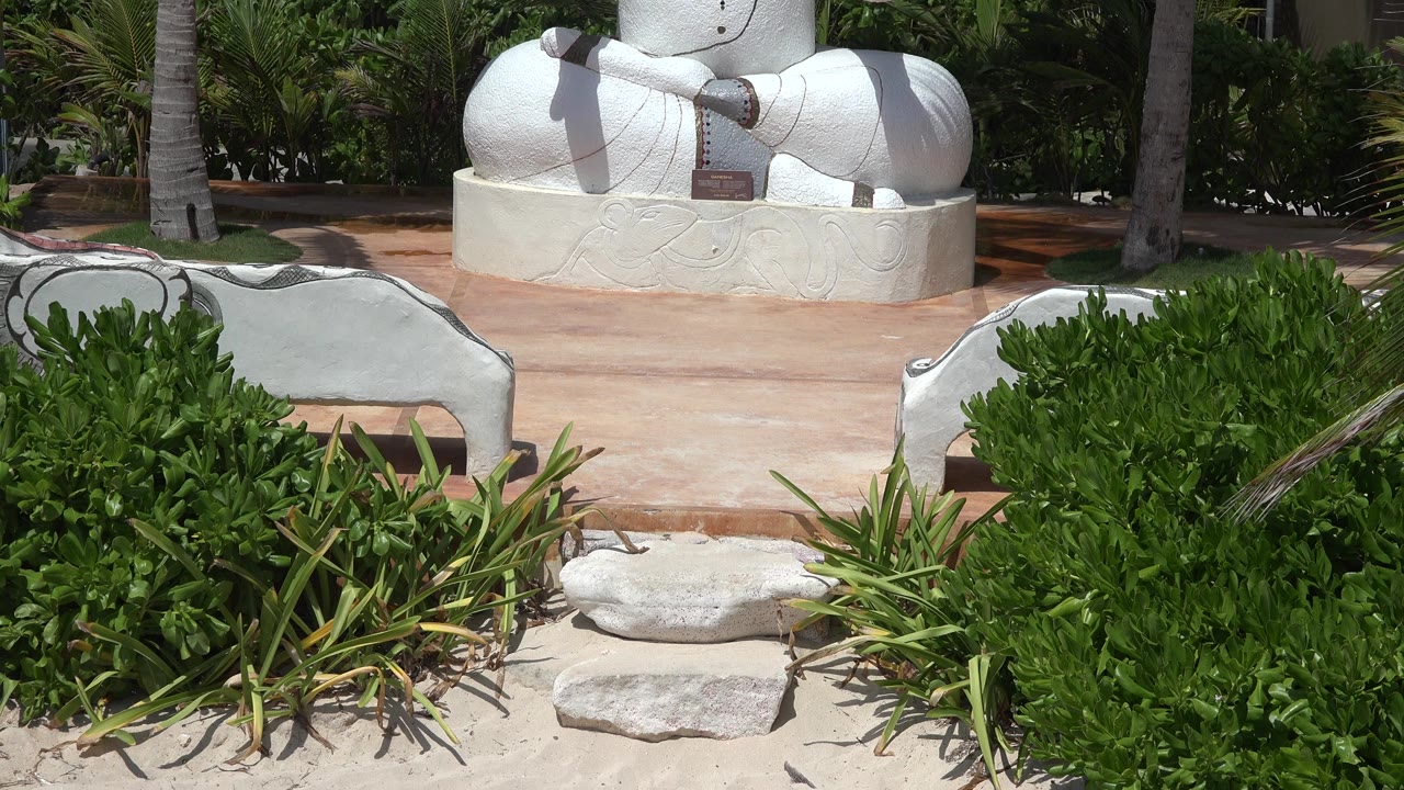 White seated statue partly hidden behind shrubs and stone edging.
