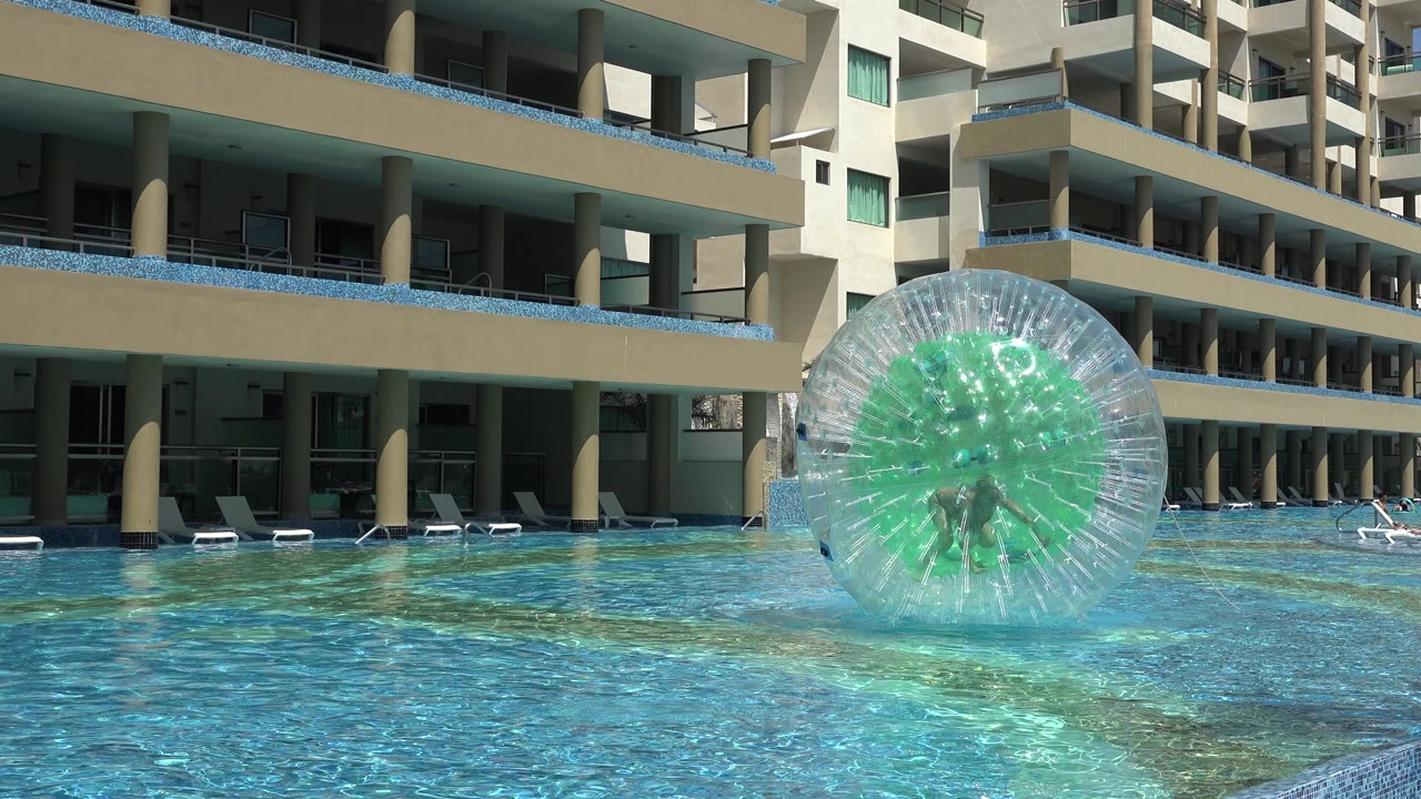 Clear inflatable ball floating in a resort pool beside hotel balconies.