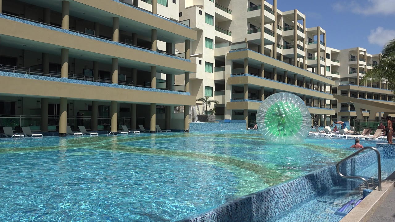 Hotel pool with a clear inflatable ball floating near resort buildings.