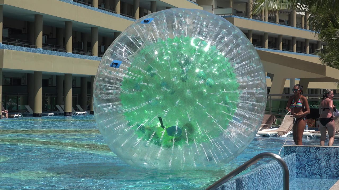Clear inflatable water ball floating in a hotel pool near guests