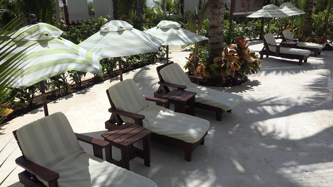 Empty lounge chairs, small tables, and striped umbrellas in hard sunlight.