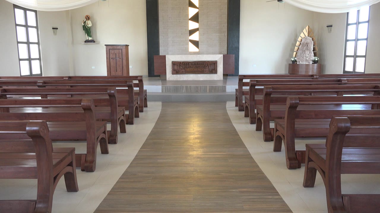 Opening view of an empty church in Playa Del Carmen, Mexico, with wooden pews framing a central aisle toward the altar and no visible people.