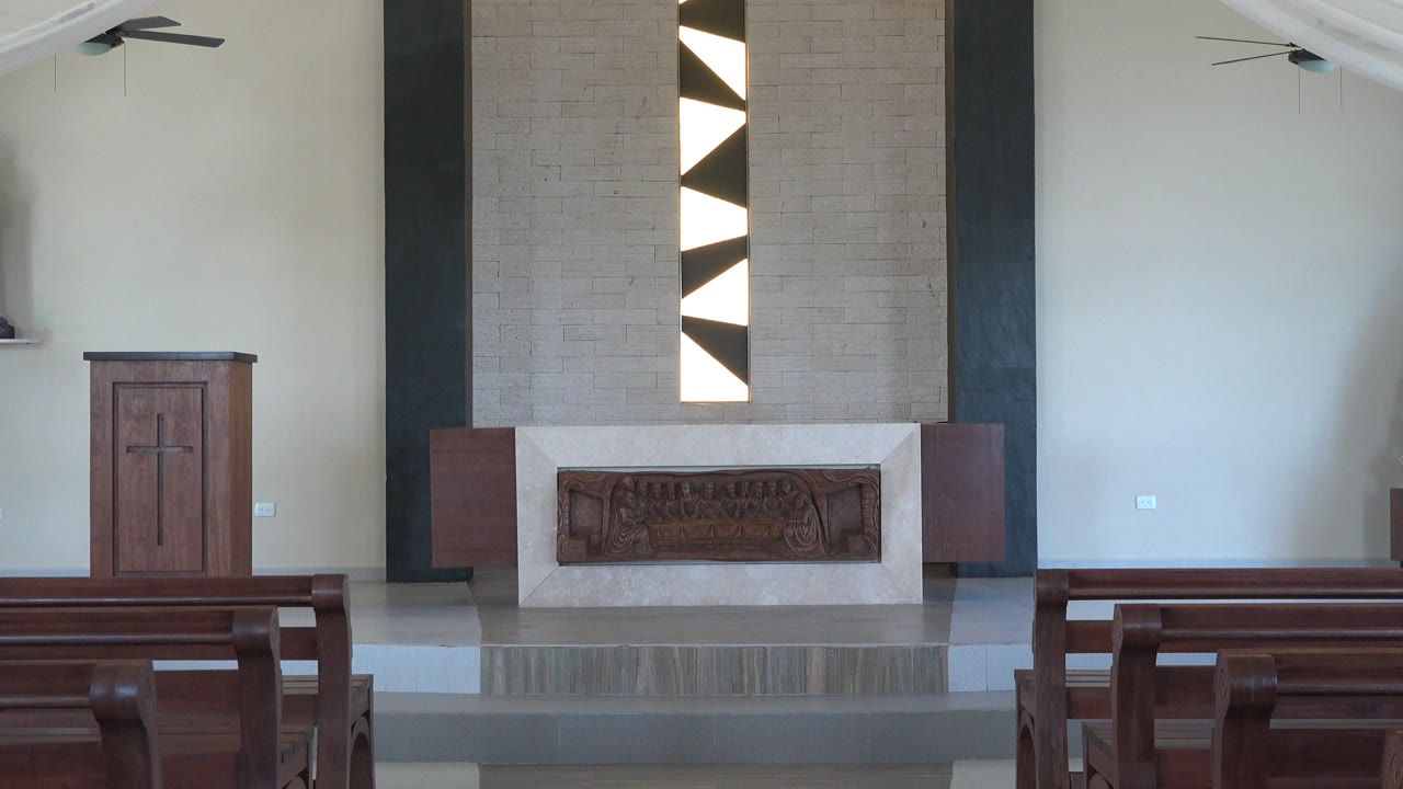 Empty church interior with pews, pulpit, altar, and geometric window panels.