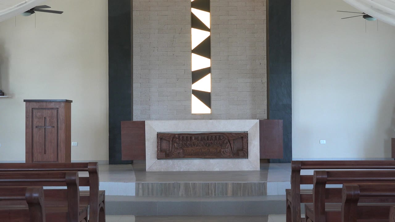 At 0:01, the Playa del Carmen church interior centers more on the altar and vertical black and white geometric windows, with pew backs across the lower frame and no visible people.