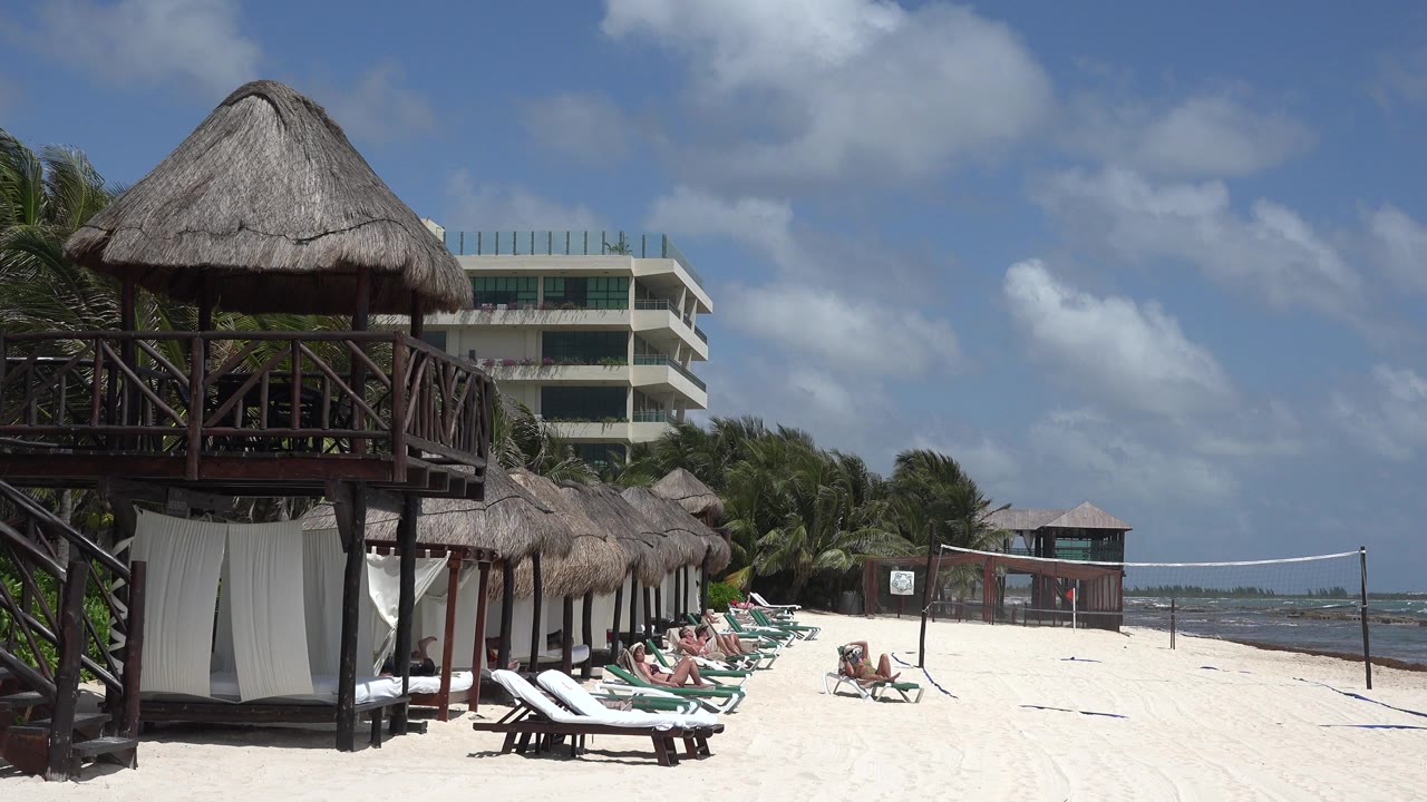 Thatched beach hut beside lounge chairs and ocean under blue sky.