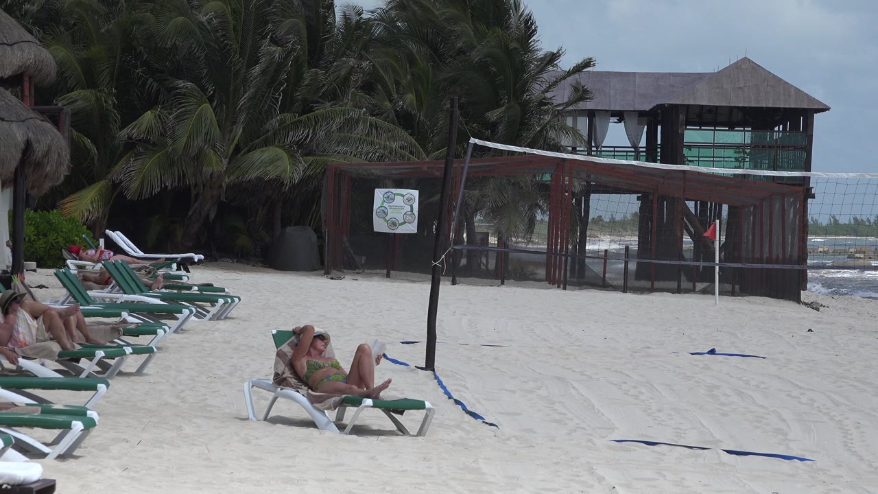 Beach volleyball net beside lounge chairs and a wooden beach building