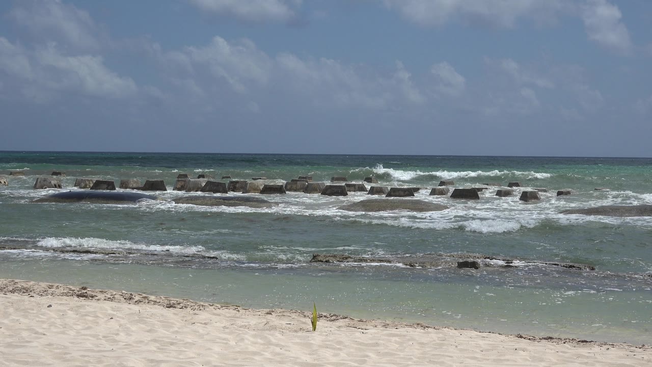 Ocean waves break over low rocks beyond a pale sandy foreground.
