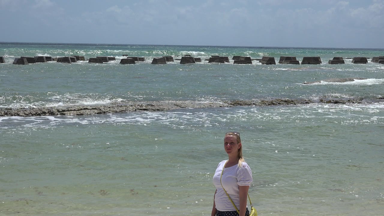 Woman in a white shirt standing near shallow ocean waves.