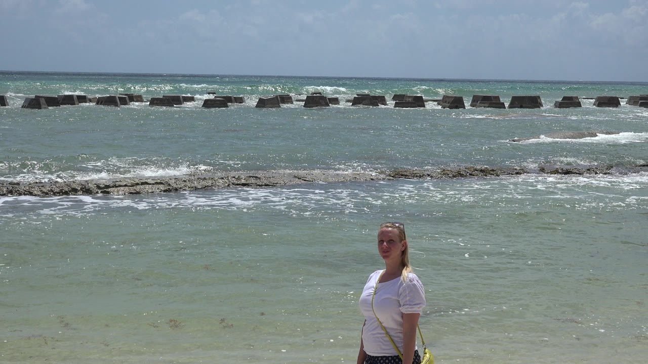 At 0:01, the woman remains near the lower center of the Playa Del Carmen shoreline as white surf gathers across the reef line in the background.