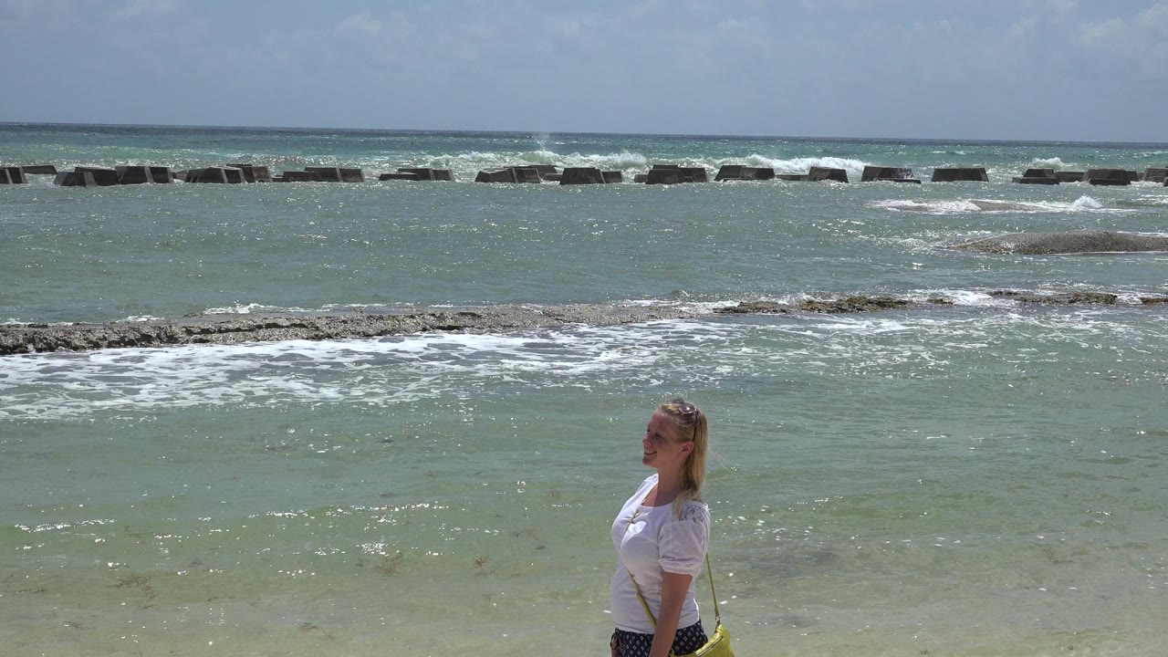 Woman in profile standing at the edge of shallow surf.