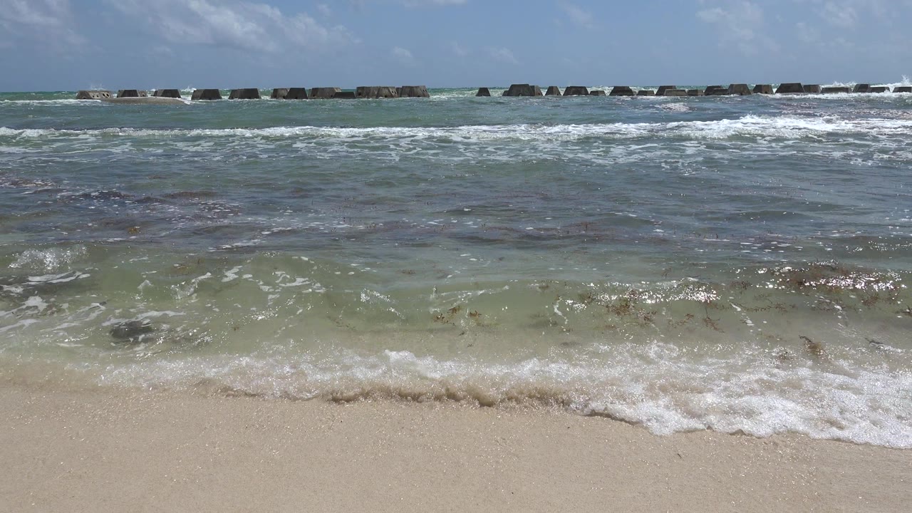 Small waves reaching a sandy beach with breakwater blocks offshore.