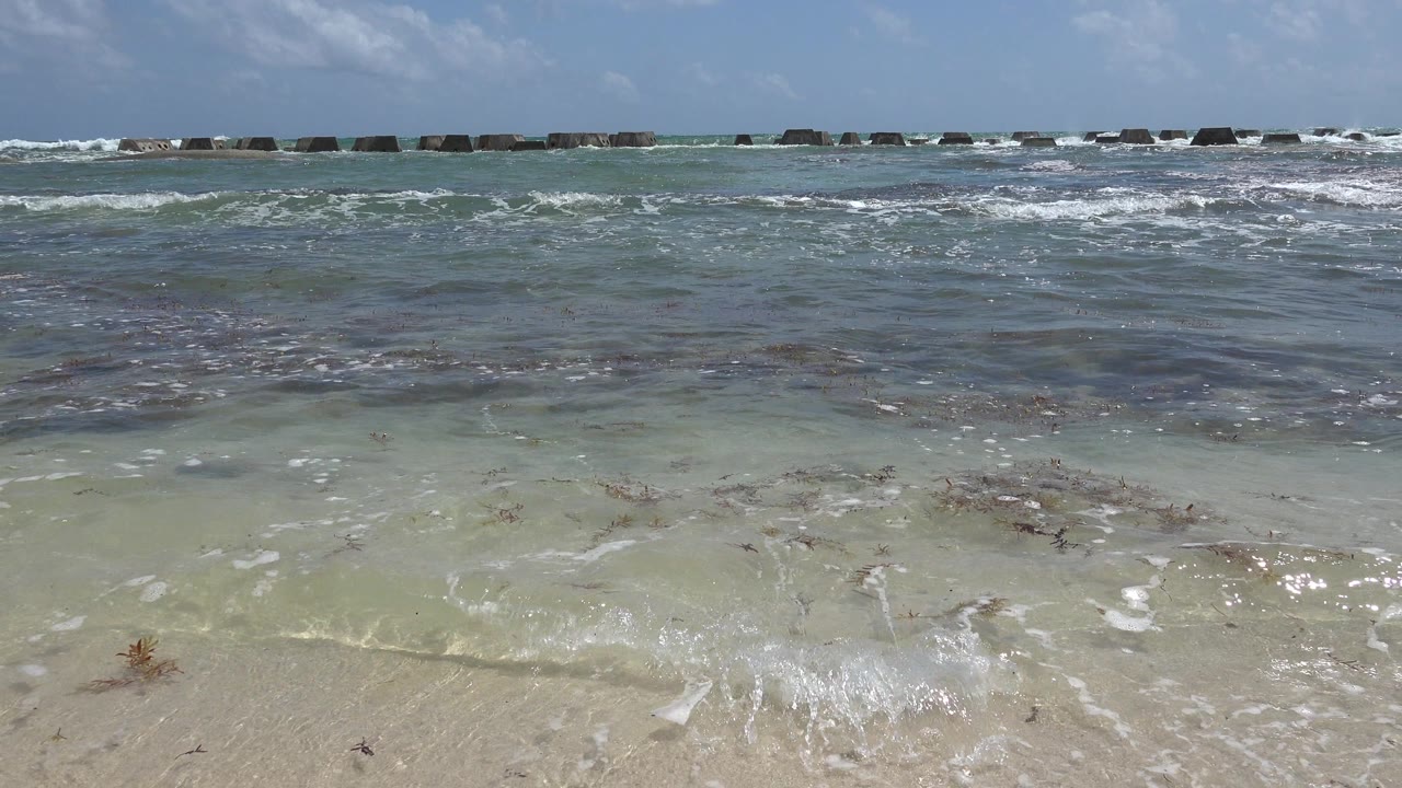 Low surf rolls toward sandy beach with rocks across the background.