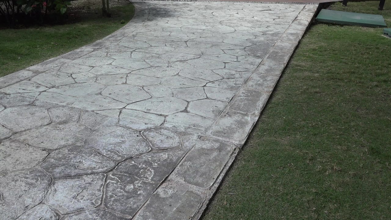 Stamped concrete walkway beside green grass and shrubs.