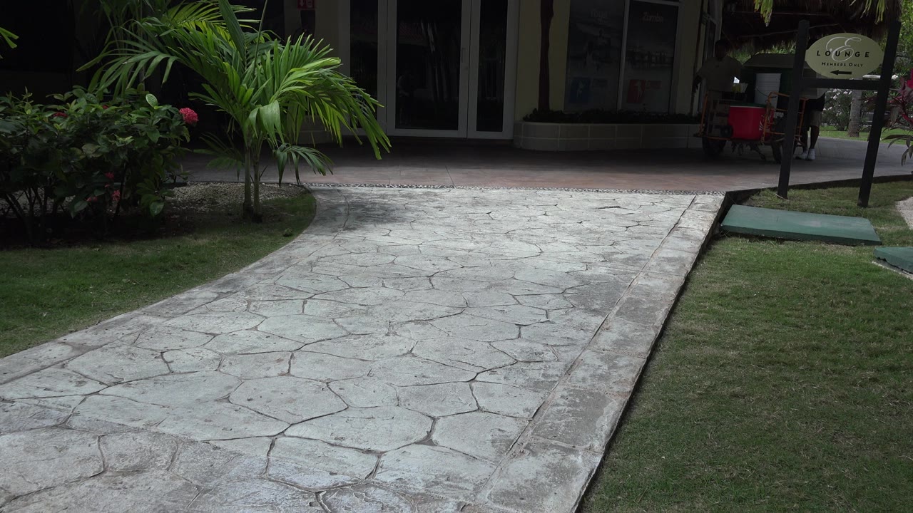 The second frame holds on the Playa del Carmen path, lawn, palms, dark building entrance, and freestanding sign, with no visible people or cart yet.