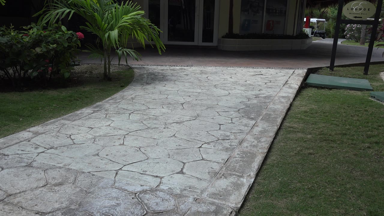 Stamped concrete walkway leading toward a shaded tropical building entrance.