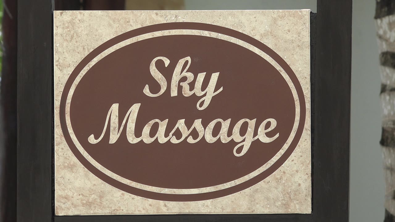 Centered Sky Massage sign in Playa del Carmen, with the right edge revealing greenery beyond the dark post and no visible people.