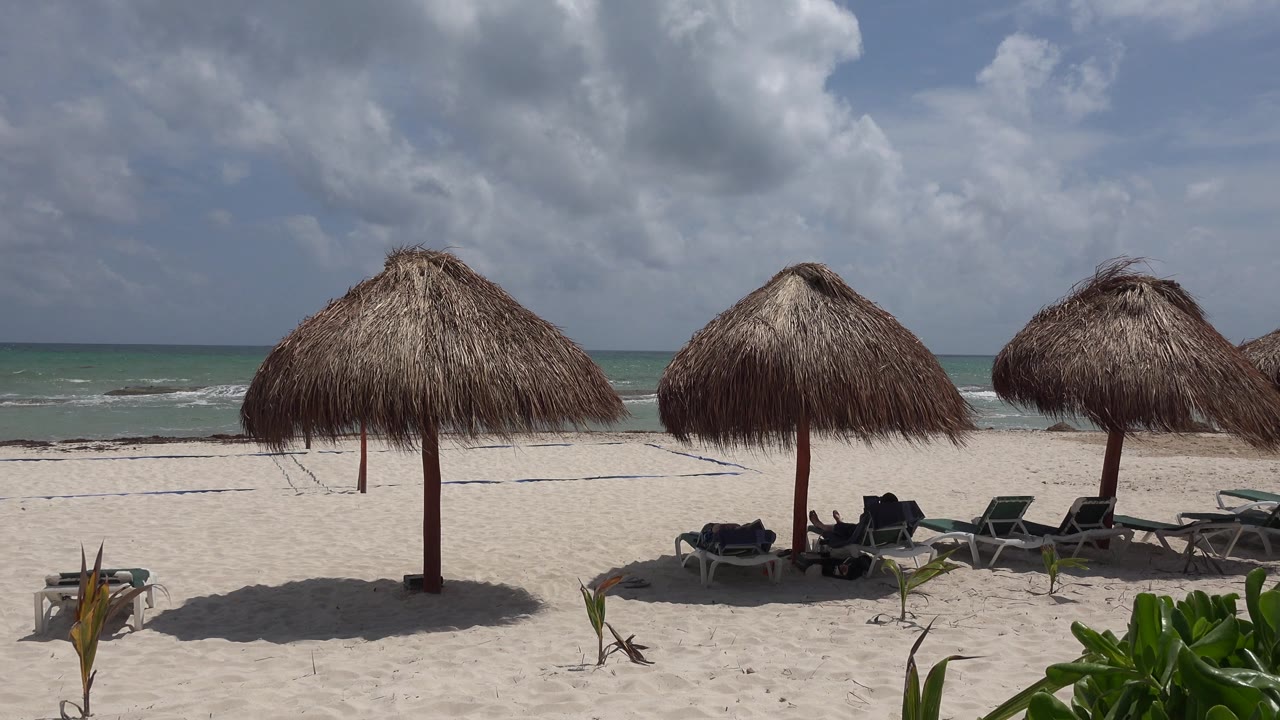 Beach chairs under thatched umbrellas with cloudy sky and turquoise water
