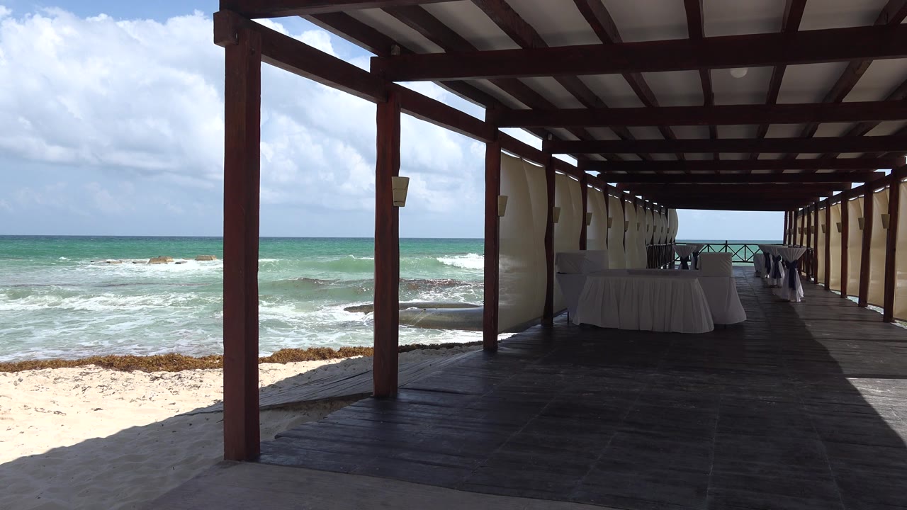 Shaded cabana deck beside ocean waves and sandy beach.