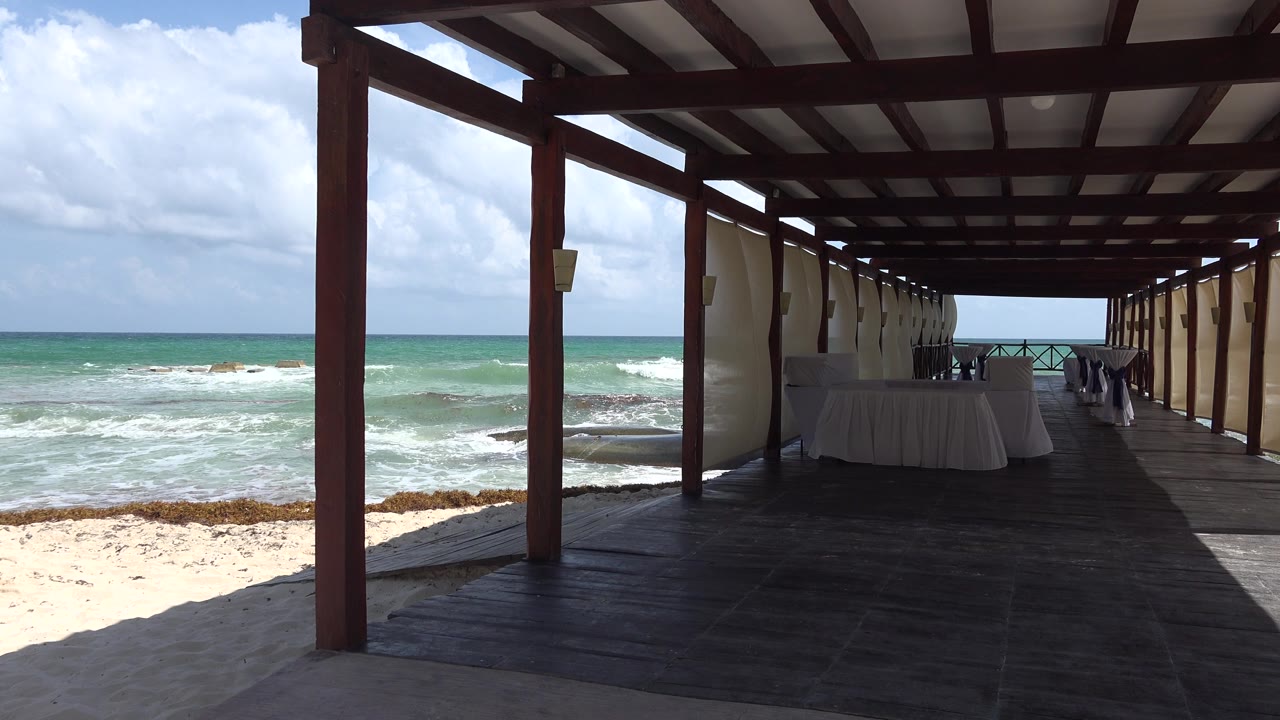 A slightly later view inside the Playa del Carmen cabana shows the dark deck leading to a railing, turquoise water, pale sand, and no visible people.