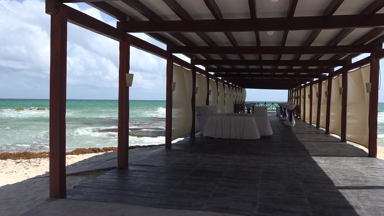 Covered beach dining walkway with ocean and sand on both sides.