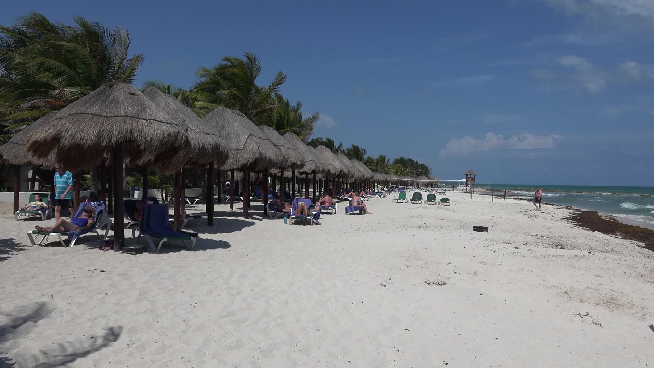 Beach cabanas, lounge chairs, people, white sand, and ocean waves.