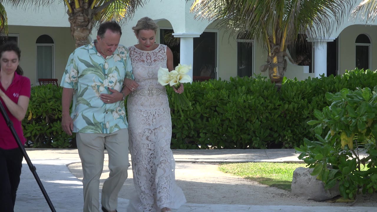 Woman in magenta shirt crosses near bride and groom outdoors.
