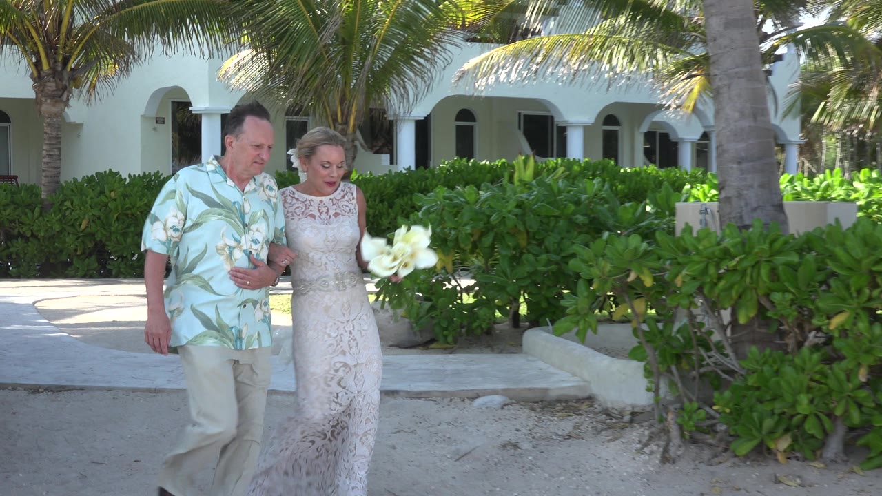 Newly married couple walking arm in arm beside palm trees and hedges.