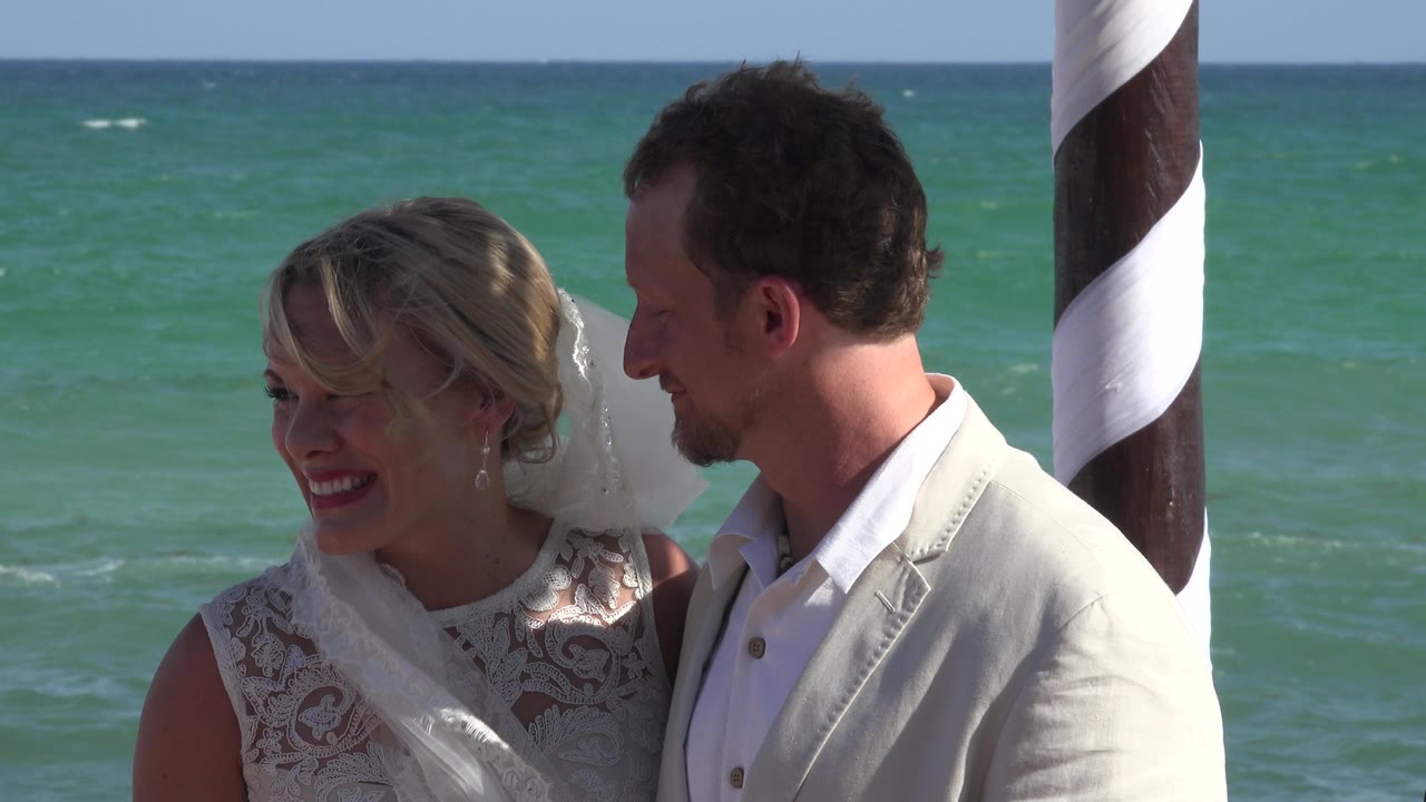 Bride and groom standing by the ocean near a striped post.