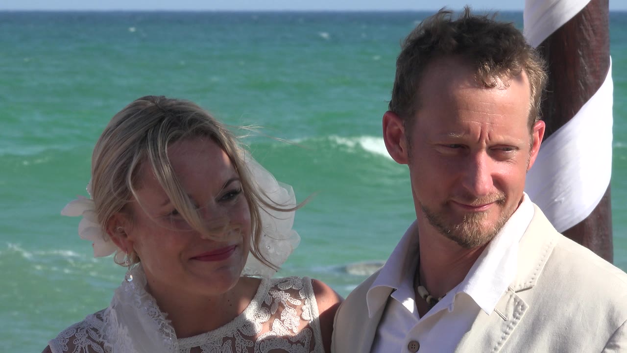 Couple standing near turquoise ocean water and striped pole.