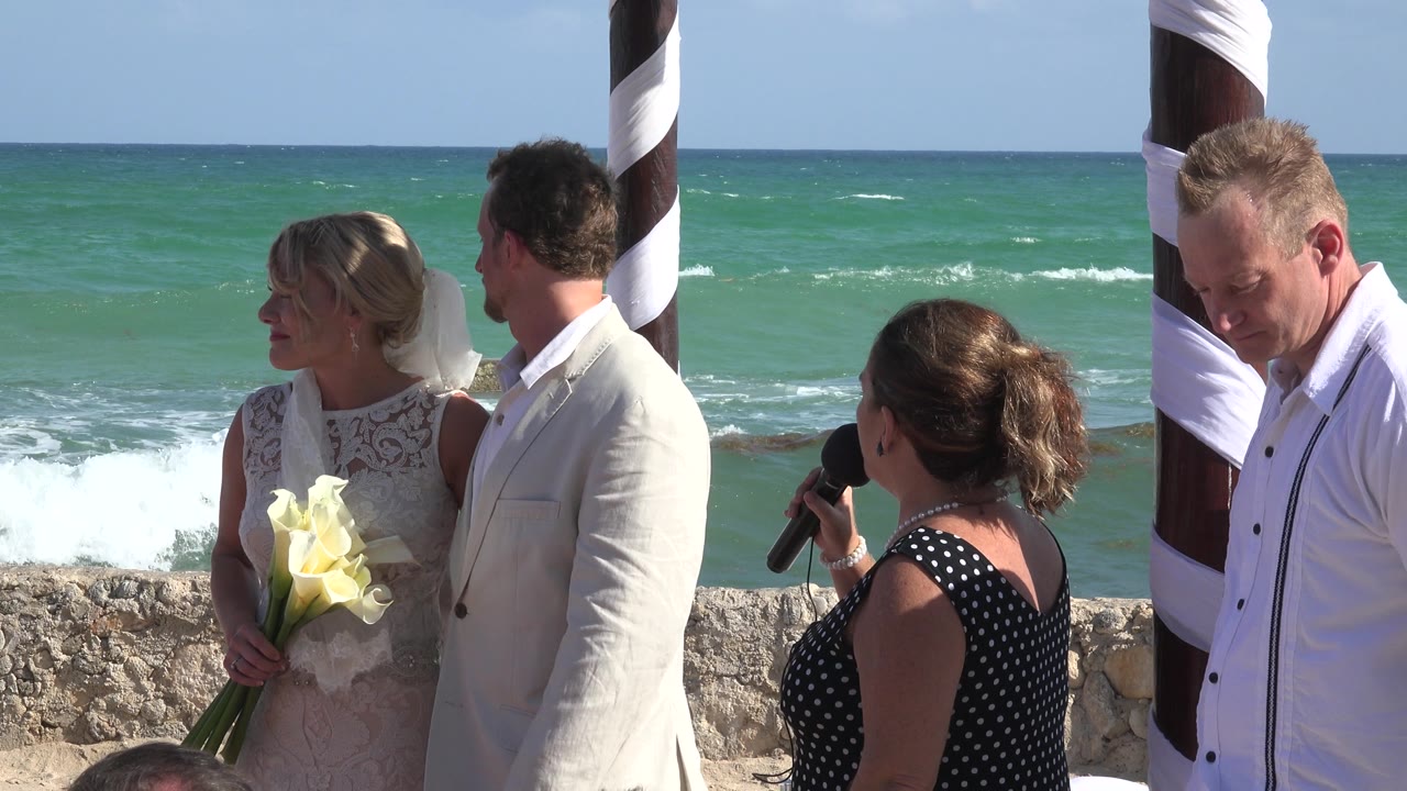 Officiant speaks to a bride and groom beside a beach seawall.