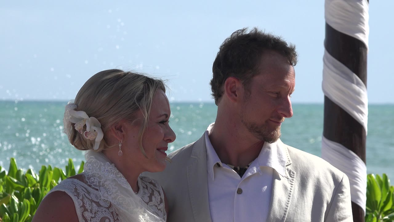 Couple standing by greenery with sea behind them.