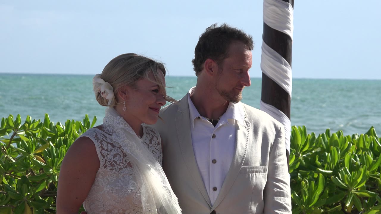 Bride and groom standing beside a striped post with ocean behind them.