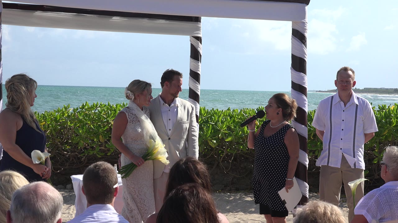 The Playa del Carmen ceremony continues as the bride and groom face the officiant, with attendants at both sides and the sea horizon visible behind the arbor.