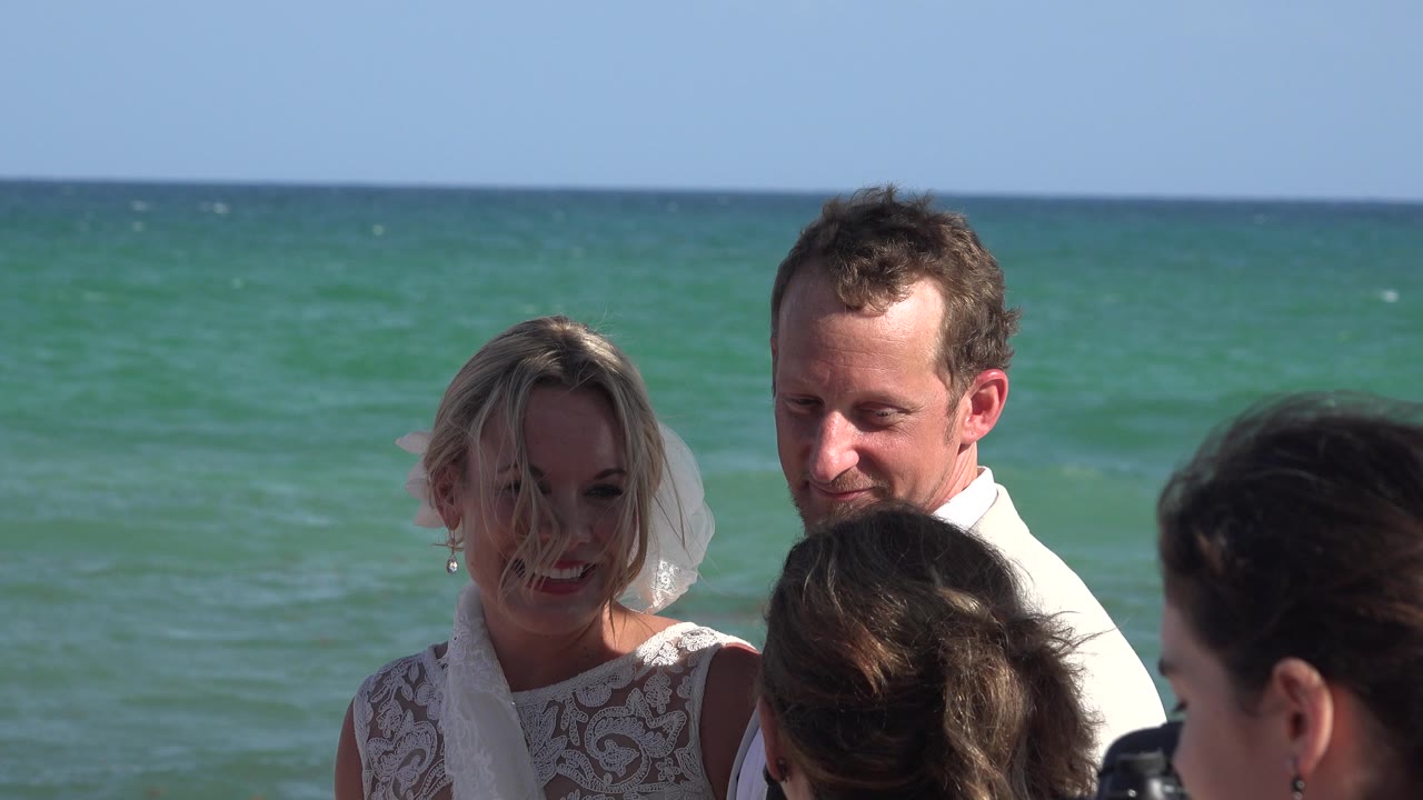 Bride and groom standing near interviewers with ocean behind them.