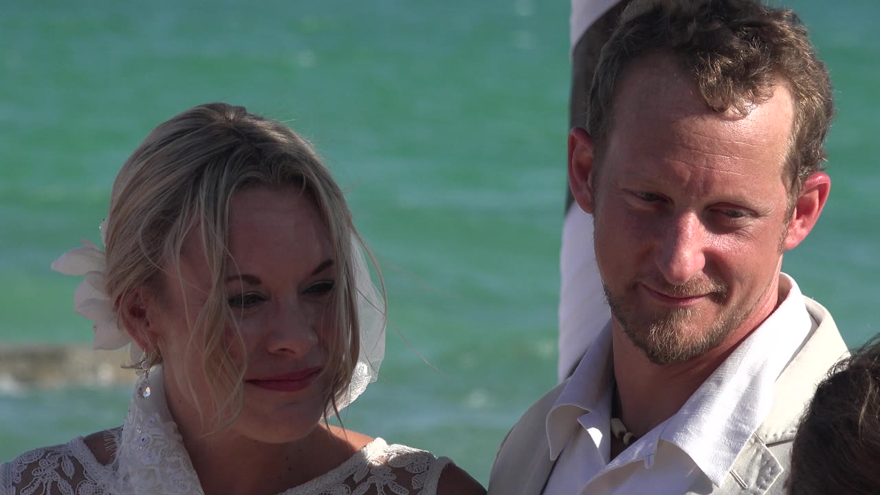 At 0:01, the couple remains framed tightly, with the woman looking down slightly and the man facing forward against the Playa del Carmen ocean backdrop.