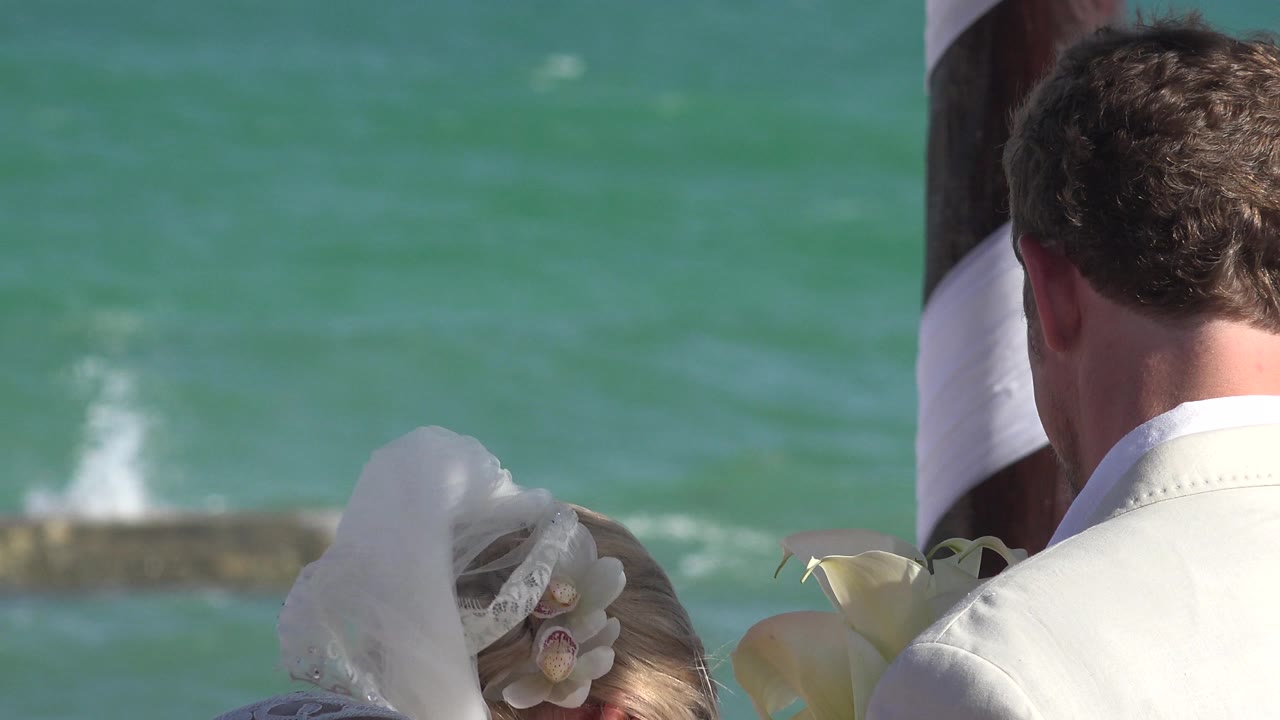 Bride and groom partly framed beside turquoise ocean water.