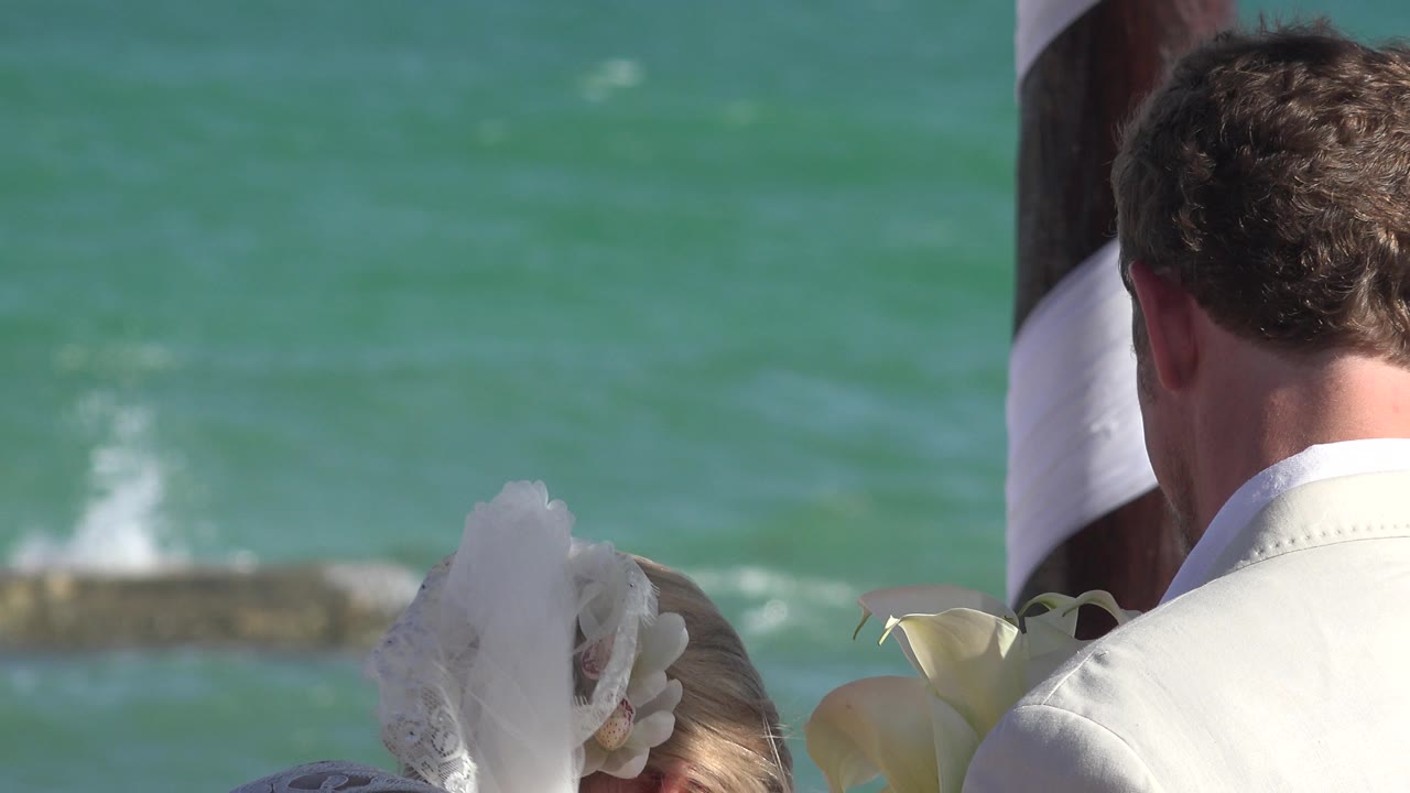 In Playa del Carmen, Mexico, the bride's white veil and the groom's shoulder remain close to the striped post, with small waves breaking behind them.