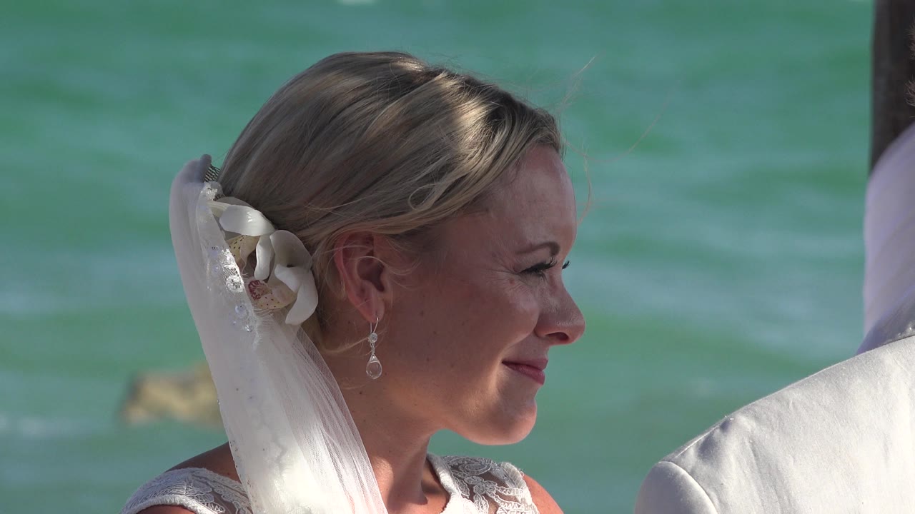 Bride in profile smiling near turquoise ocean water.