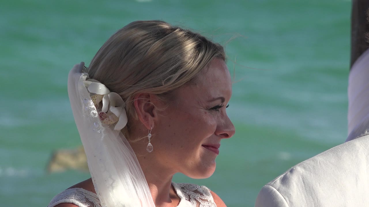 At 0:01, the bride remains in profile in Playa del Carmen, with the white veil and hair flowers clearer against the blue-green water behind her.