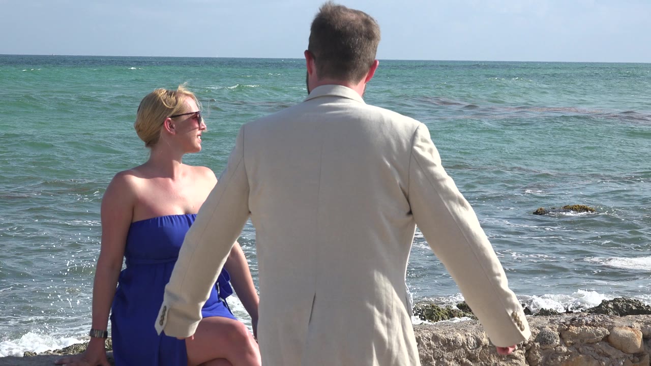 Well-dressed couple beside ocean water and rocks.
