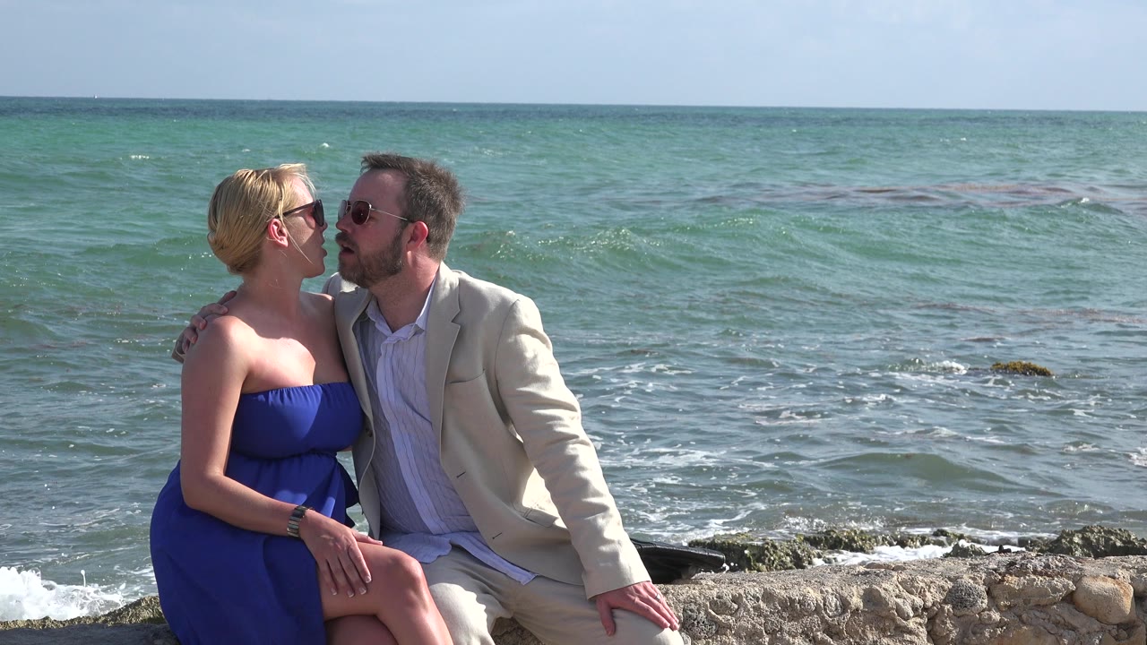 Couple sitting together by the ocean on a stone edge.