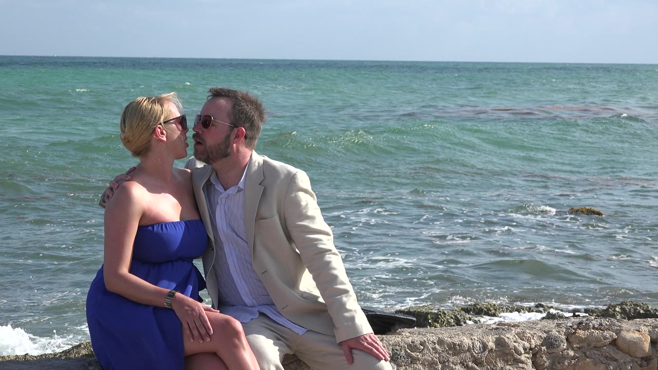 At 0:01 in Playa del Carmen, Mexico, the seated couple lean closer together while the green-blue water fills most of the background.