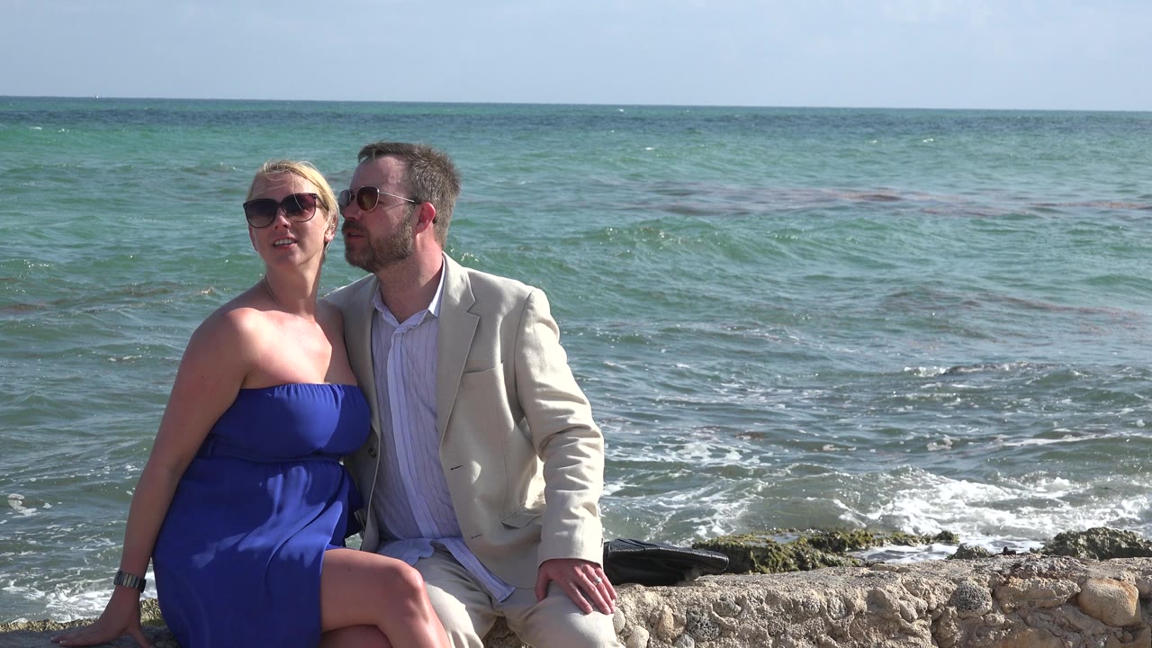 Couple sitting on a stone edge with ocean behind them.